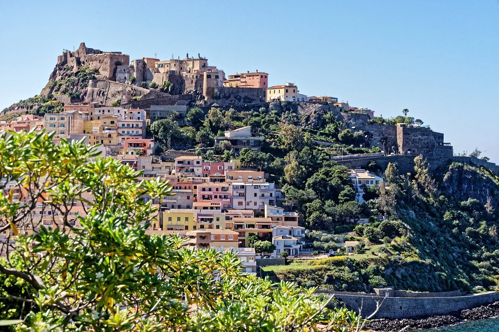 Il borgo di Castelsardo con le case colorate sul pendio del promontorio e il Castello dei Doria in cima, sotto un cielo azzurro
