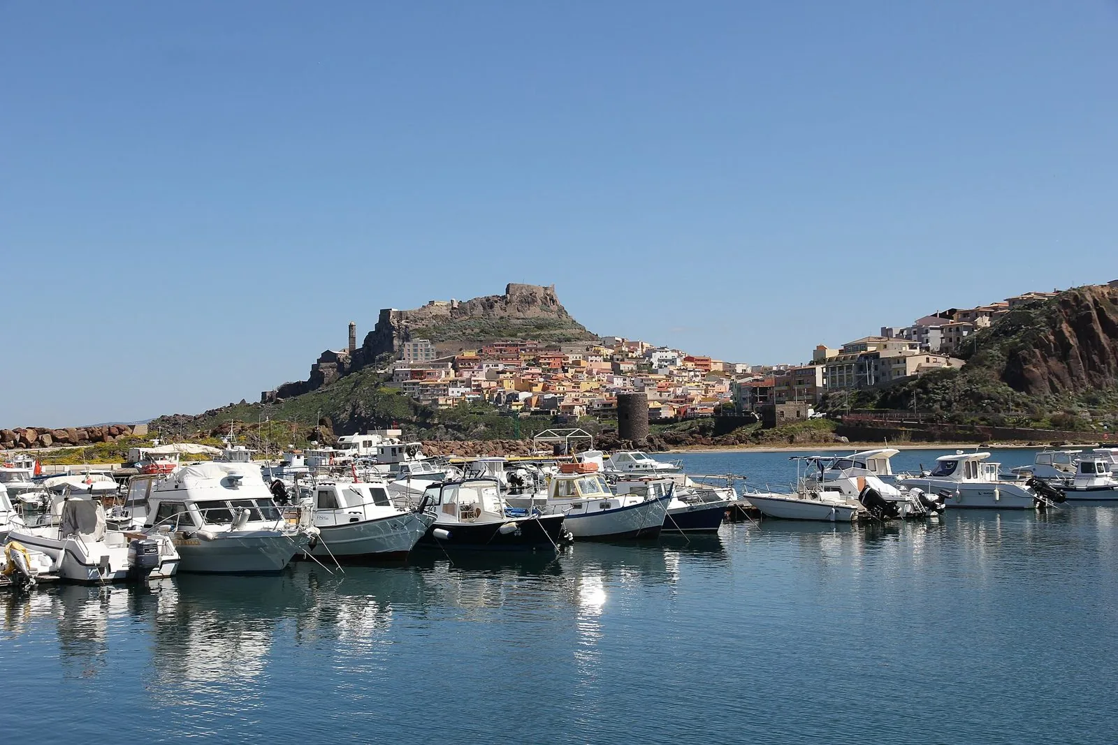 Il borgo colorato di Castelsardo con il castello in cima al promontorio, visto dal porticciolo con le barche ormeggiate
