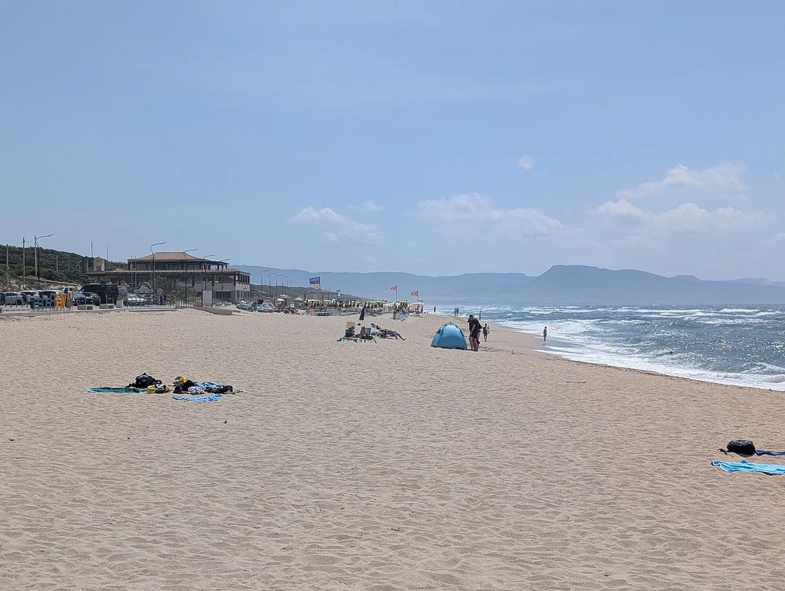 Spiaggia di Li Mindi a Badesi: ampia distesa di sabbia chiara, mare mosso a destra e rilievi della costa sullo sfondo