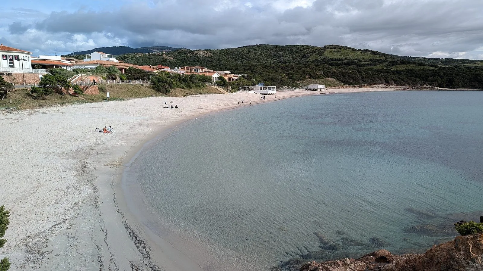 La spiaggia Longa dell'Isola Rossa, un arco di sabbia chiara con acqua bassa e trasparente e le colline di macchia sullo sfondo